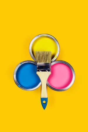 Renovation concept. Yellow background with three color paint jars and one brush. Flat lay, top view....