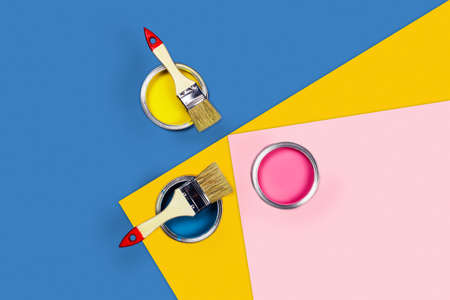 Renovation concept. Tricolor blue, yellow, pink background with three paint jars and brushes. Flat lay, top view, copy space.の写真素材
