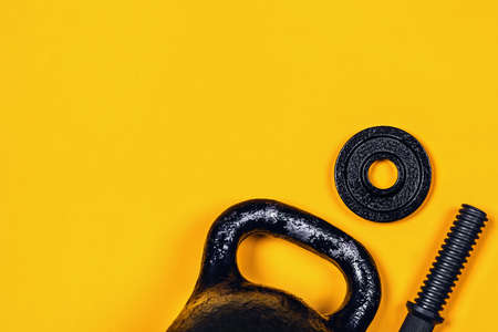 Sports background. Kettlebell and dumbbell on yellow background. Flat lay, top view, copy space.の写真素材