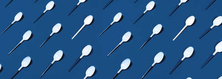 Pattern of white plastic spoons located on classic blue background. Flat lay, top view.の写真素材