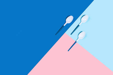 Dangerous and needed three plastic spoons. Environmental problem of plastic rubbish pollution. Three-color background: classic blue, pink and blue. Flat lay, top view, copy space.の写真素材