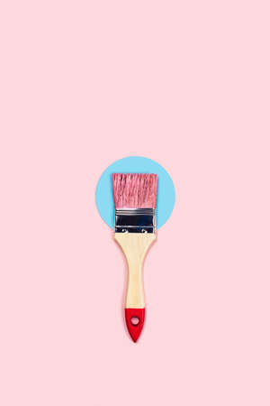 Renovation picture. Pink background with one pain brush located on blue circle, central composition. Flat lay, top view, copy space.の写真素材