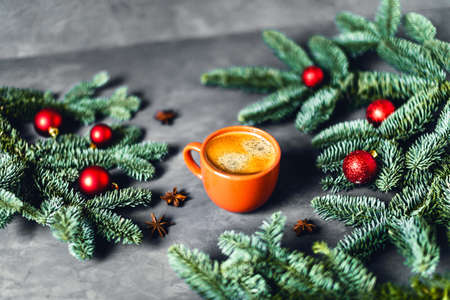 Christmas composition - tasty coffee in orange cup on gray background surrounded by red Christmas cheers and green spruce branches.の写真素材