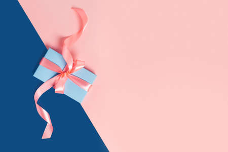 Greeting card with one gift box on classic blue background. Pink bows. Central composition. Flat lay, top view.の写真素材