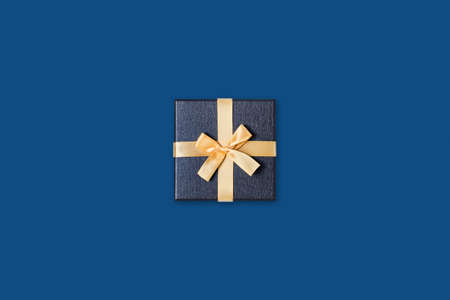 Holiday card. Grey gift box with gold bow on classic blue background. Flat lay, top view, copy space.の写真素材