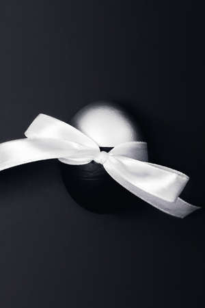 One black and silver Easter egg with bow on dark grey background. Flat lay, top view, copy space.