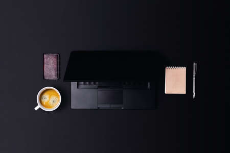 Modern workspace in dark color with laptop, coffee, notepad and pen. Central composition.の写真素材