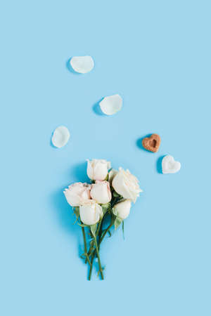 Vertical morning card. White roses on a blue background with scattered petals and two pieces of sugar in the shape of hearts.の写真素材