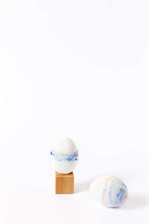 Vertical Easter picture. Two watercolor-painted eggs on a wooden cube and on a white table.の写真素材