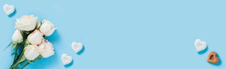 White roses on a blue background with pieces of sugar in the shape of hearts.の写真素材