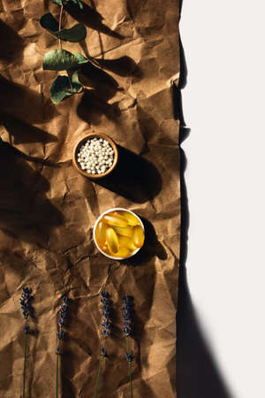 View from above on fish oil capsules and homeopathic balls lying on crumpled wrapping paper. Surrounded by sprigs of eucalyptus and lavender.の写真素材