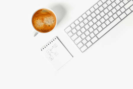 Home office. A white desktop with a keyboard, notepad and a cup of delicious coffee.の写真素材