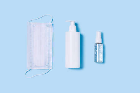 Flat lay with a medical mask placed in the center, a bottle of antiseptic soap and a hand sanitizer.