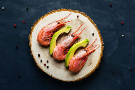 Three king shrimps lying on a wooden platter surrounded by avocado and hot peppers.の写真素材