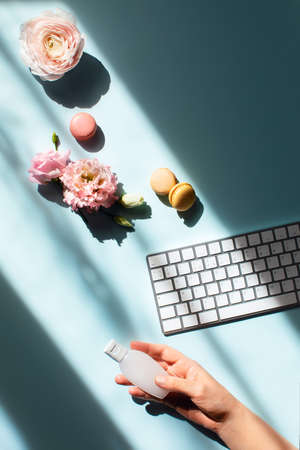 Flat lat with flowers and macaroons in sunlight and with a sanitizer on a women hand. Hygiene and preventive measures in the workplace.の写真素材