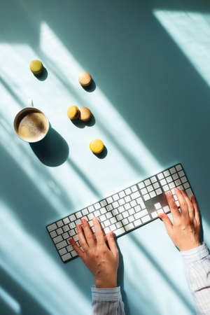 Workplace at home by the window. Flat lat with cup of coffee and macaroons in sunlight and women hands typing on the keyboard.の写真素材