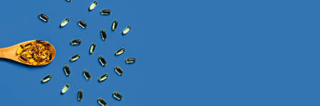 Medical classic blue background. Fish oil capsules in a wooden spoon. Flat lay, top view.の写真素材