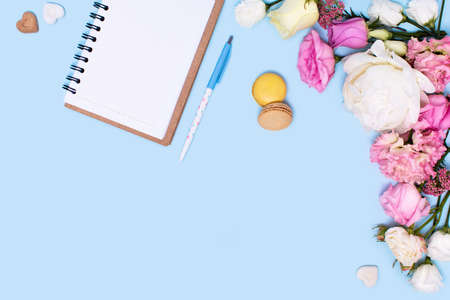 Greeting card or invitation to a holiday or party. Roses and peonies, notepad, pen and macaroni cakes with sugar peaces on a blue background.の写真素材