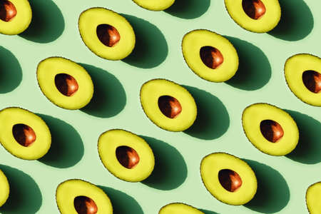 Avocado cut in half in sunlight. Neo mint green backgrount. Front view.の写真素材
