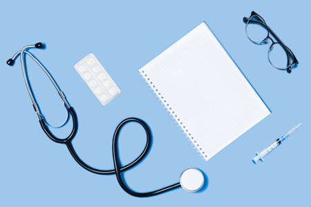 Medical blue background with different accessories: stethoscope, syringe notepad and glasses.の写真素材