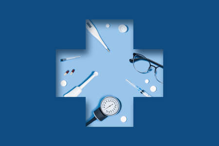 3D paper cut out art. Medical classic blue background with syringe, tablets, thermometer, stethoscope, glasses lying in a carved medical cross.の写真素材