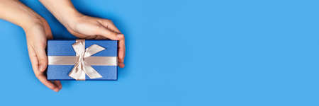 Web banner with women's hands holding a box with a gift or surprise on a grey background.