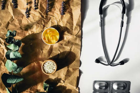 Flat lay with fish oil capsules, homeopathic balls and stethoscope lying on crumpled wrapping paper. Surrounded by sprigs of eucalyptus.の写真素材