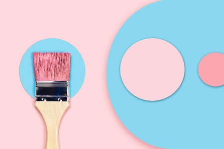 Brush stained with pink acrylic paint lying on a blue paper circle on a pink background. Abstract...