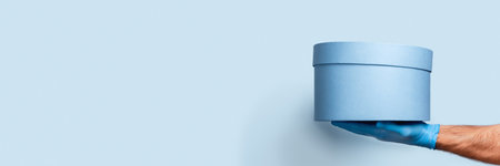Panorama wih Mans hand in latex glove and blue box with a gift inside. Remote safe delivery.