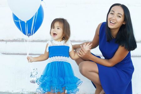 happy mom with daughter in blue dresses on a summer walkの写真素材