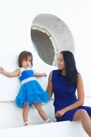happy mom with daughter in blue dresses on a summer walkの写真素材
