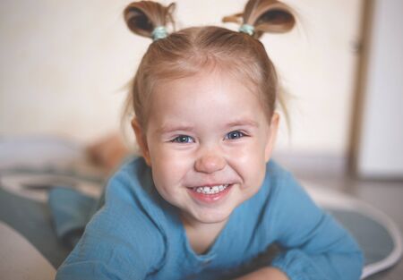 blue-eyed blonde girl in a vintage blue dress smiling.