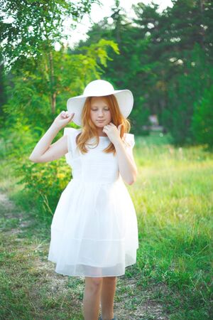 red-haired girl in a white dress and hat walks in the park.の写真素材