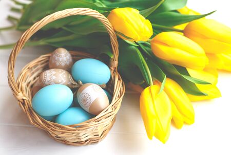 basket with vintage easter eggs and a bouquet of yellow tulips on a white background.の写真素材