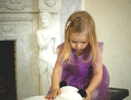 Little girl in a lavender dress playing with a soft toy.の写真素材