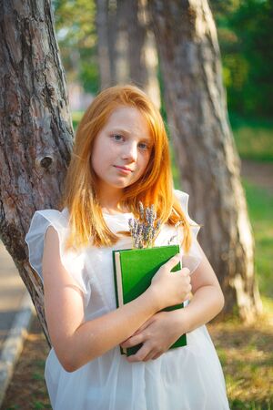 Red-haired girl in a white dress with books.の写真素材