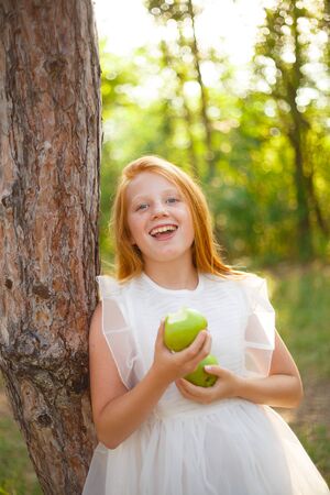 red-haired girl in a white dress with a green apple in her hands.の写真素材