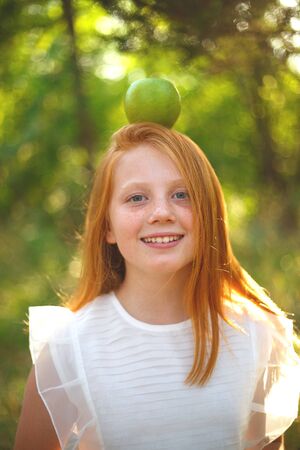 red-haired girl in a white dress with a green apple on her head.の写真素材