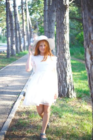 red-haired girl in a white dress and hat walks in the park.の写真素材