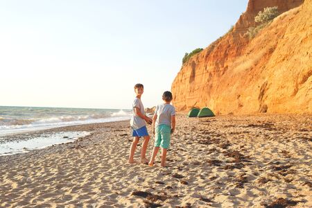 two friends are walking on a sandy beach at sunset.の写真素材
