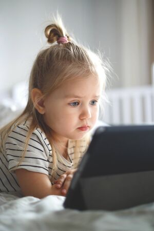 little girl at home watching tablet computer. home schooling, distance learning.の写真素材