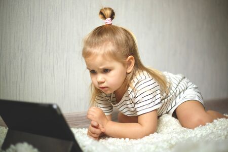 little girl at home watching tablet computer. home schooling, distance learning.の写真素材