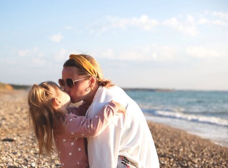 mom and daughter hug and kiss on the beach at sunset.の写真素材