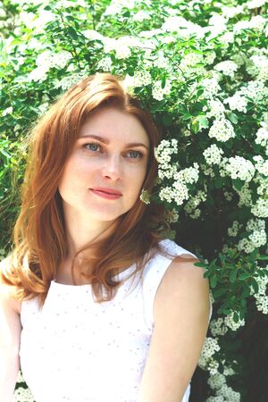 beautiful red-haired woman with freckles surrounded by white flowers.の写真素材