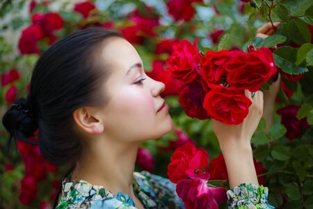 brunette woman smiling in a flowering bush of red roses.の写真素材