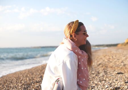 mom and daughter hug and kiss on the beach at sunset.の写真素材