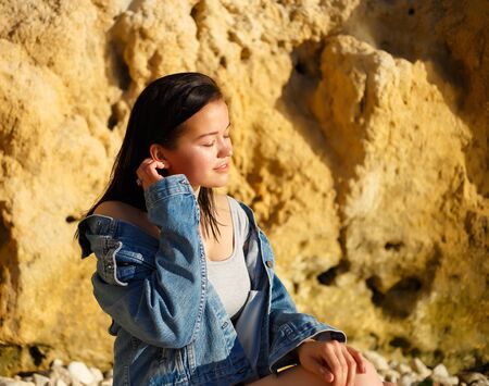 portrait of a woman in a denim jacket on a background of yellow rock.の写真素材