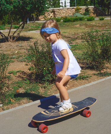 Little cute girl rides a big skateboard in the park.の写真素材