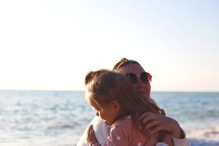 mom and daughter hug and kiss on the beach at sunset.の写真素材