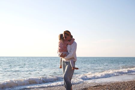 mom and daughter hug and kiss on the beach at sunset.の写真素材